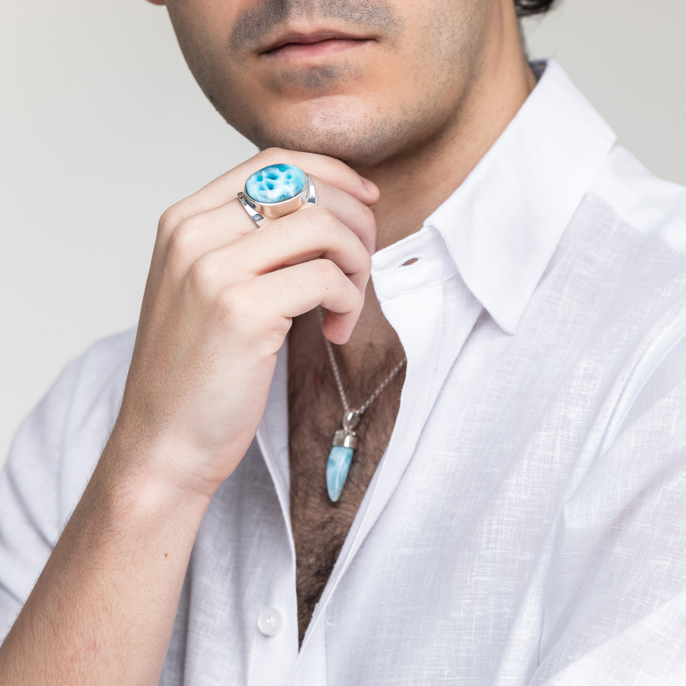 Close-up of a man wearing a polished silver Larimar ring and a Larimar pendant necklace, styled with a white linen shirt.