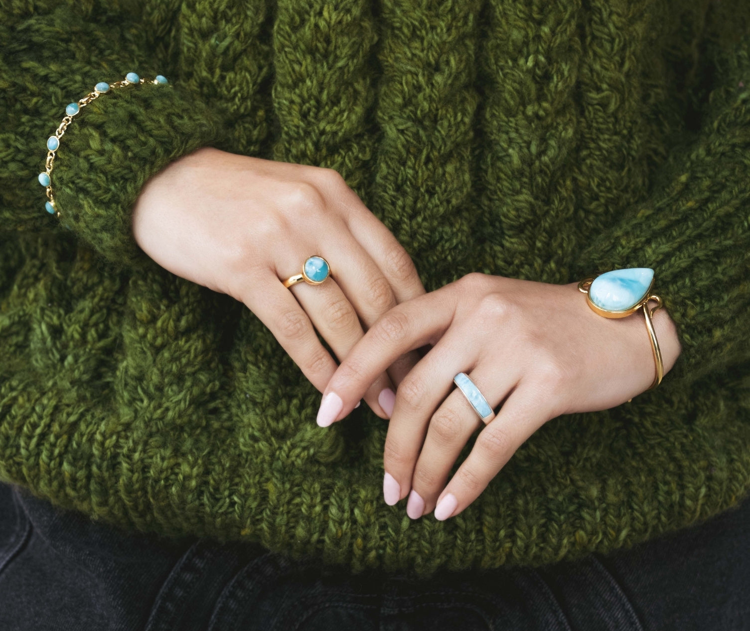 Close-up of hands wearing Larimar gemstone jewelry on a green knitted sweater background