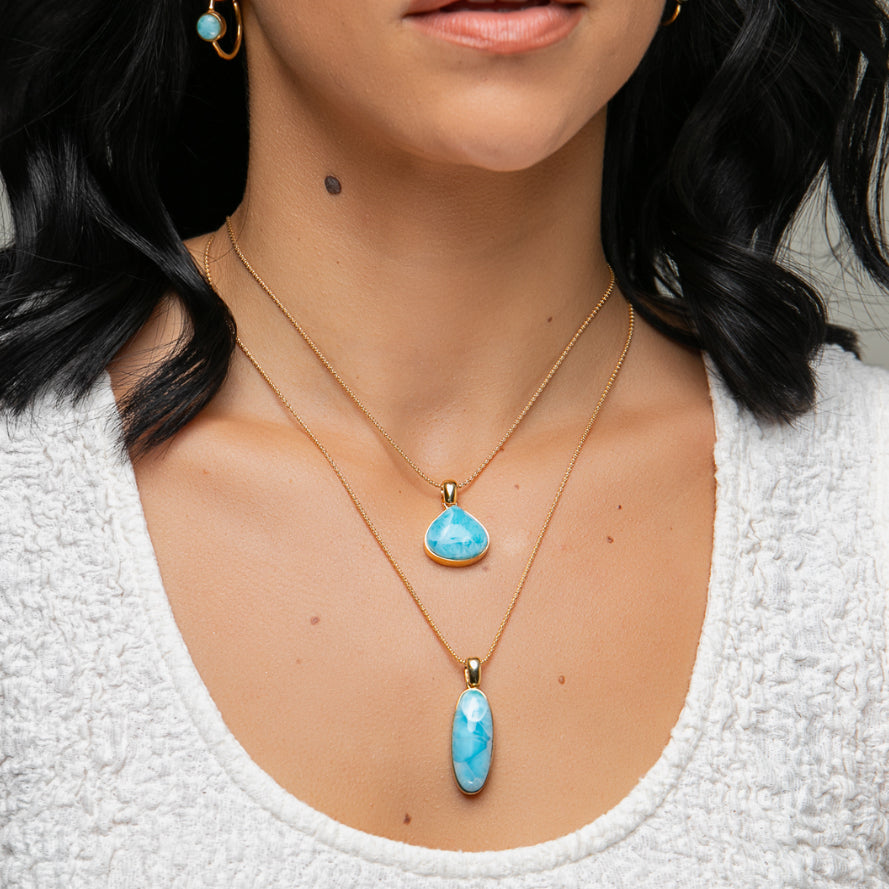 Close-up of a person wearing two Larimar  pendant necklaces and earrings.