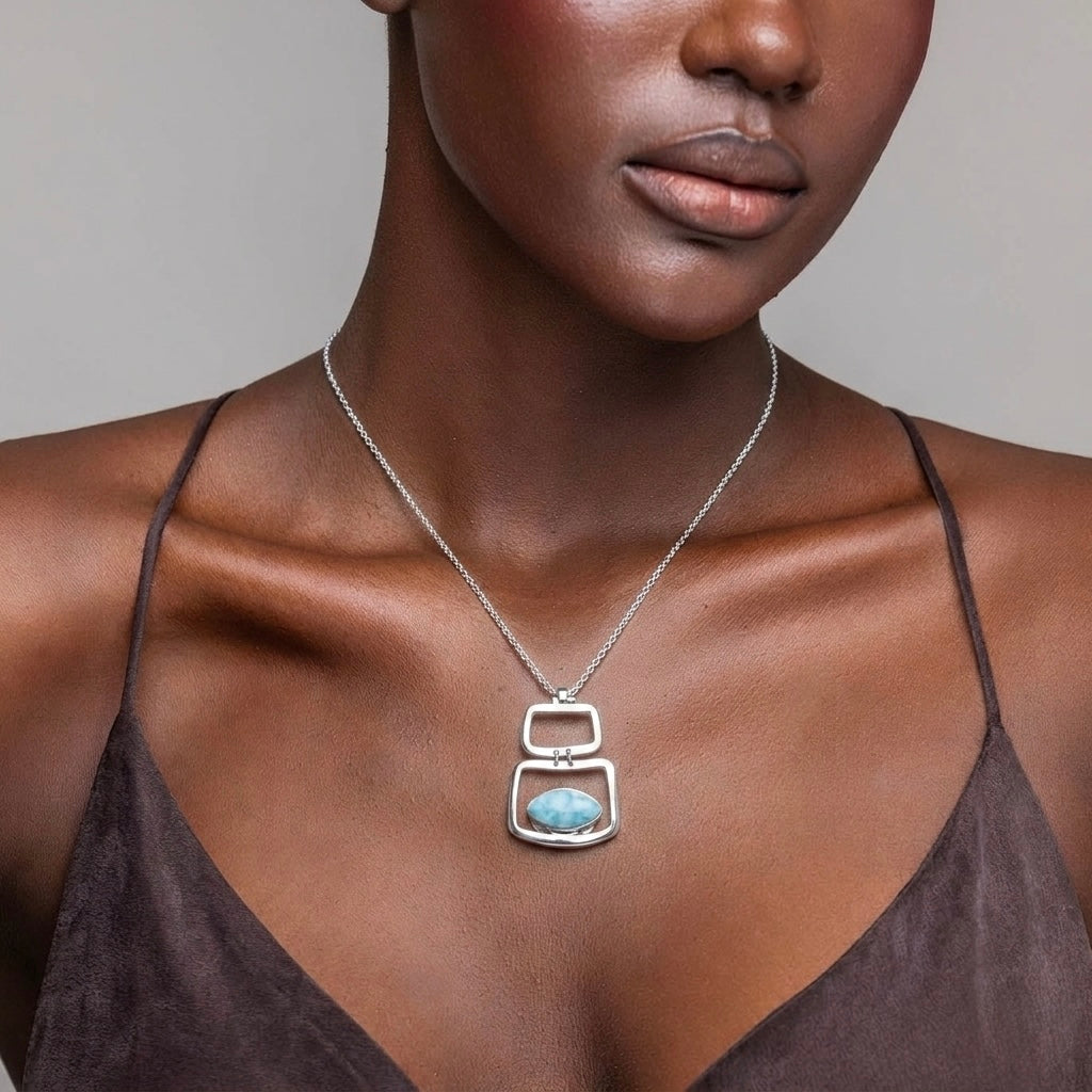Woman wearing a silver necklace with a Larimar pendant on a neutral background