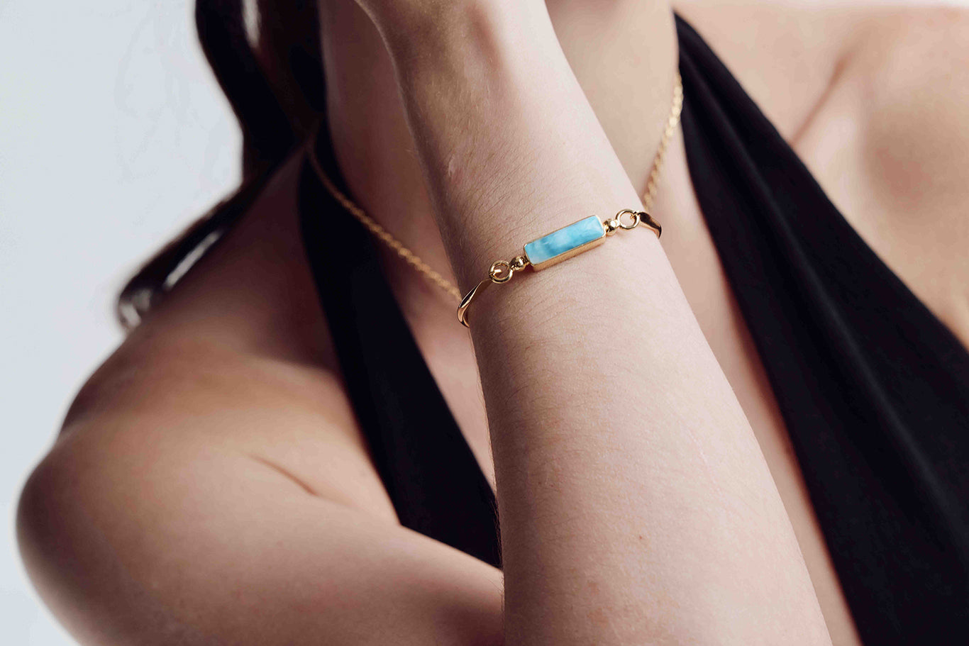 Close-up of a person wearing a gold bracelet with a Larimar blue stone on a neutral background