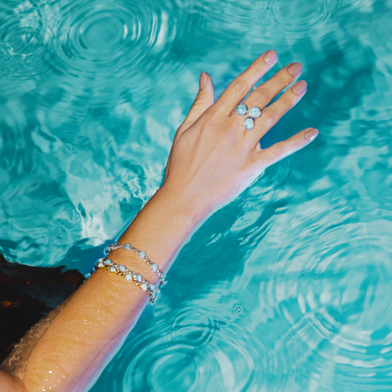 Hand with a Larimar ring and Larimar stone bracelet in clear blue water.