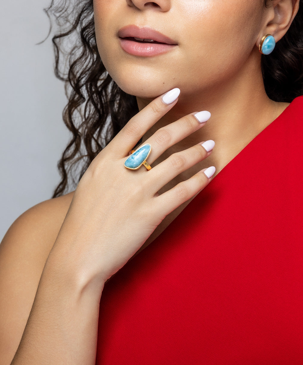 Woman wearing a Larimar stone ring and earrings on a red background