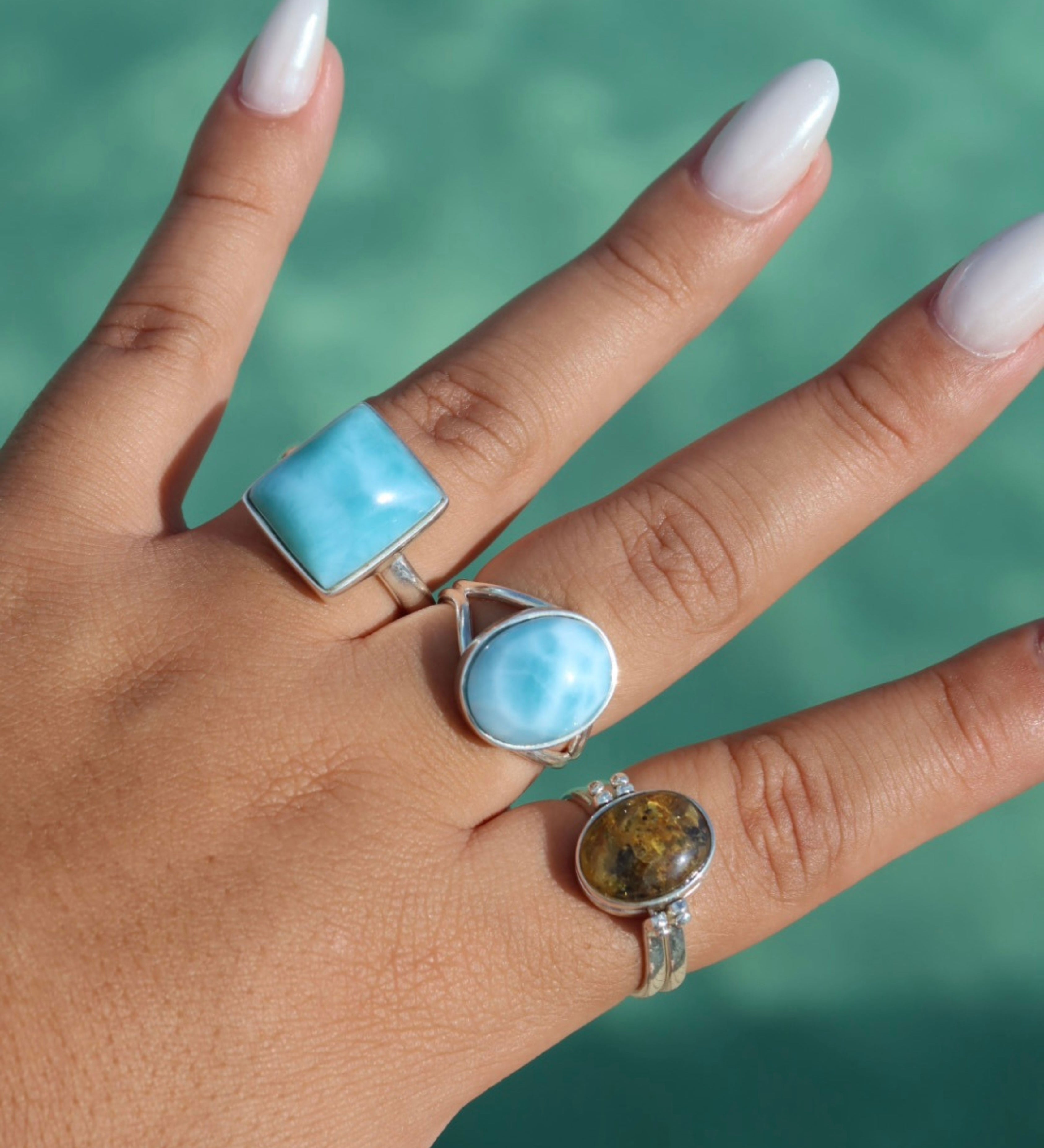 Assorted larimar rings displayed on a sandy beach, showcasing the unique blue hues and intricate designs of the gemstones against a natural coastal backdrop.