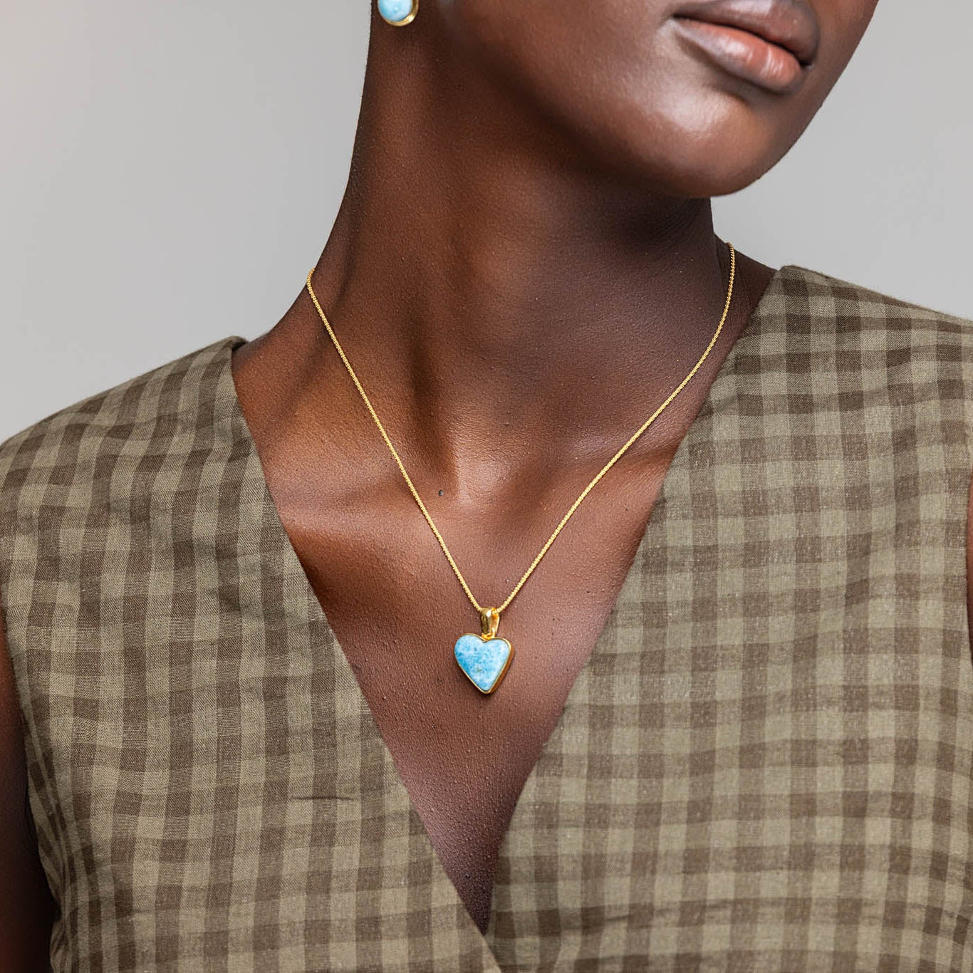 Woman wearing a gold necklace with a heart-shaped Larimar blue pendant against a neutral background