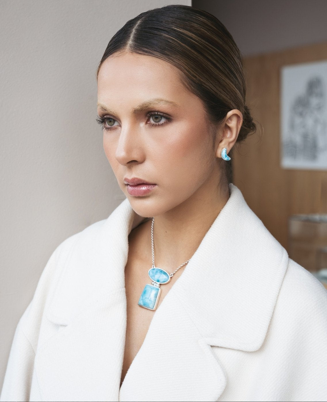 Woman wearing a white coat and blue Larimar jewelry indoors