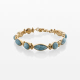 A gold bracelet featuring a row of oval-shaped Larimar blue stones, displayed on a clean white background with a soft reflection.
