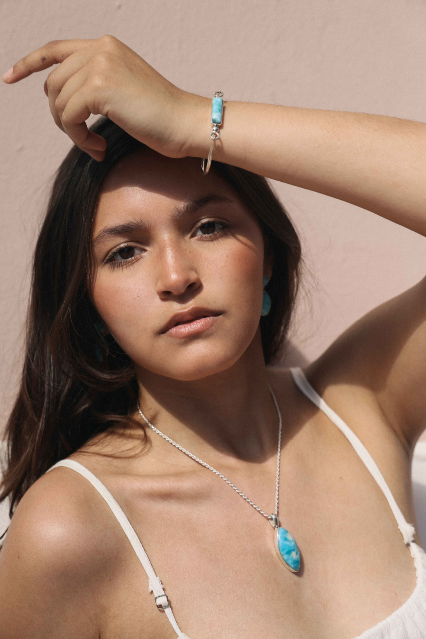 Woman wearing a white top and Dominican Larimar jewelry against a pink background.