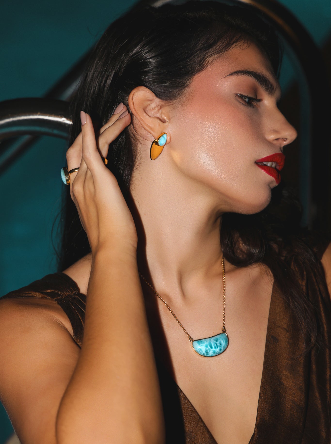 Woman wearing gold Larimar earrings and a Larimar gold necklace against a dark background.
