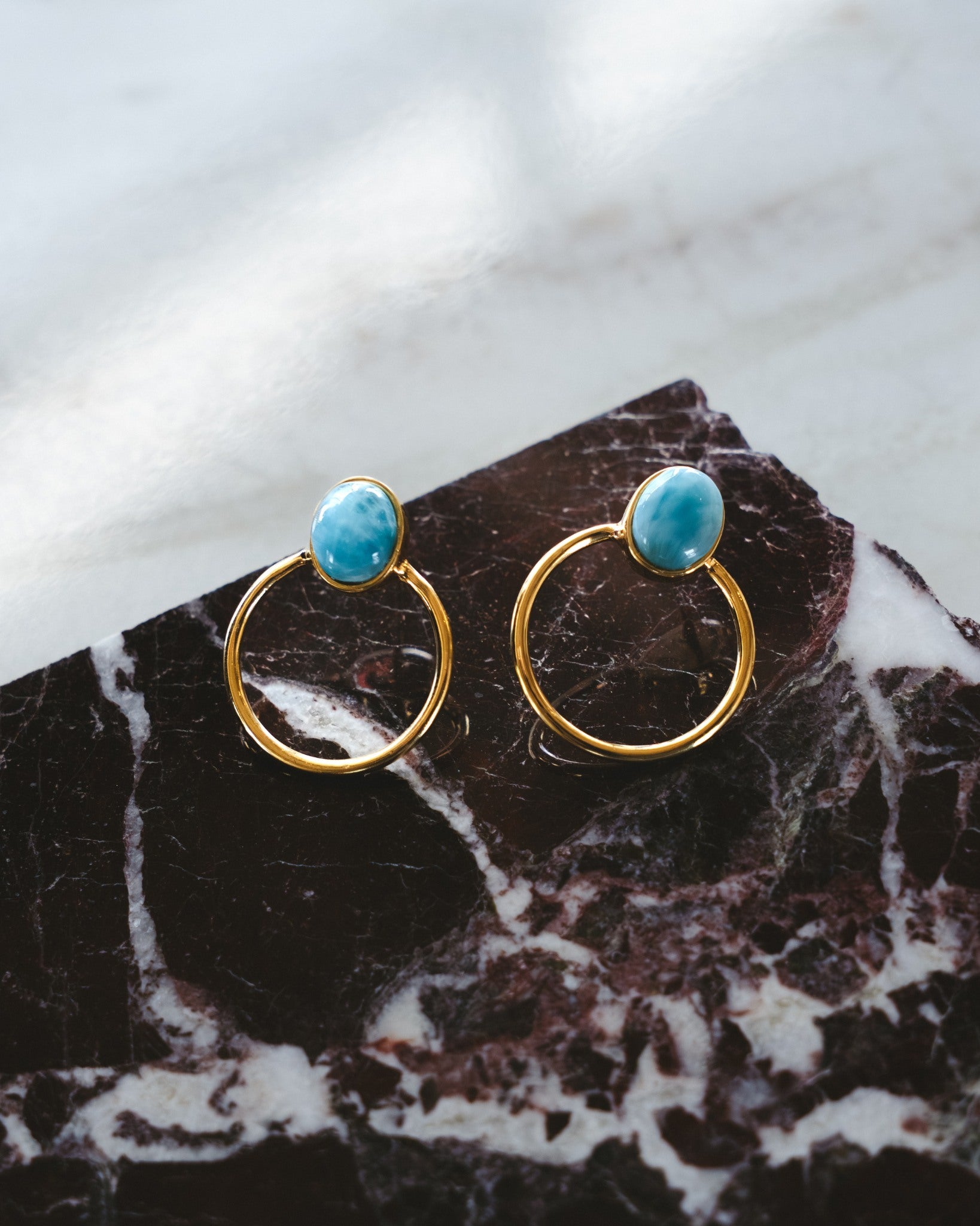 Gold hoop earrings with Larimar stones on a marble surface