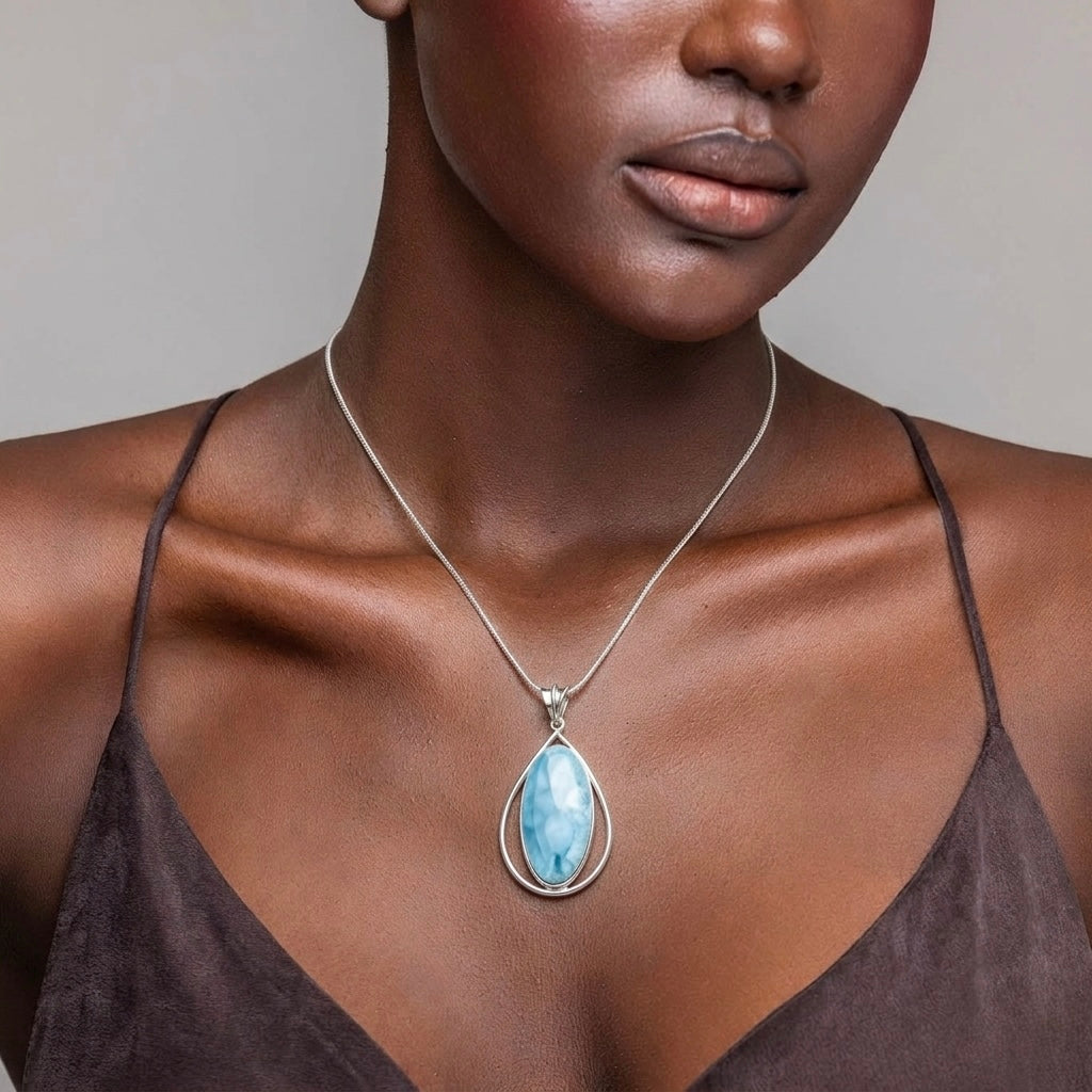 Woman wearing a necklace with a blue Larimar pendant against a neutral background