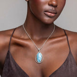 Woman wearing a necklace with a blue Larimar pendant against a neutral background