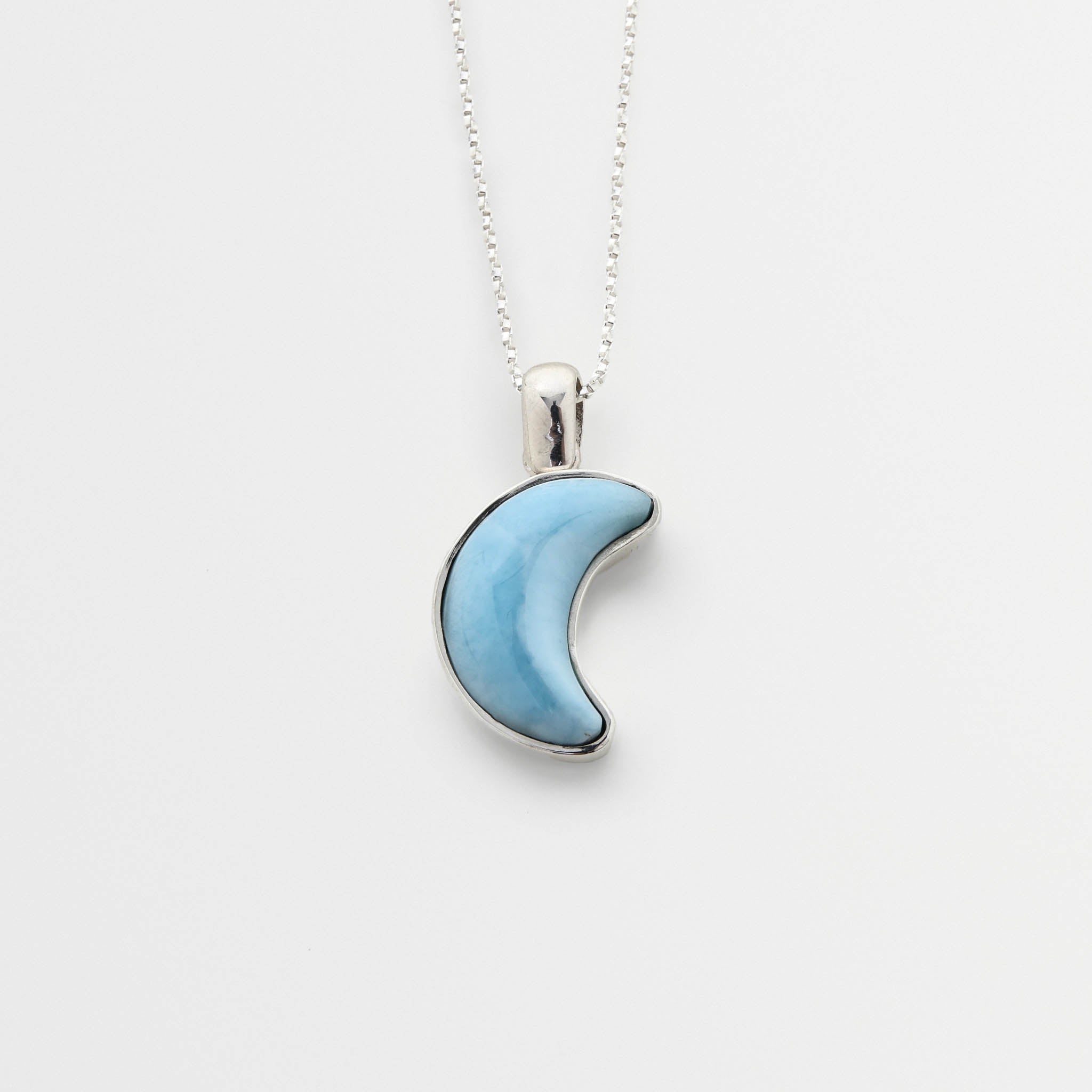 Blue Larimar crescent moon pendant on a silver chain against a white background