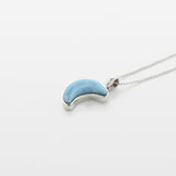 Blue Larimar crescent moon pendant on a silver chain against a white background