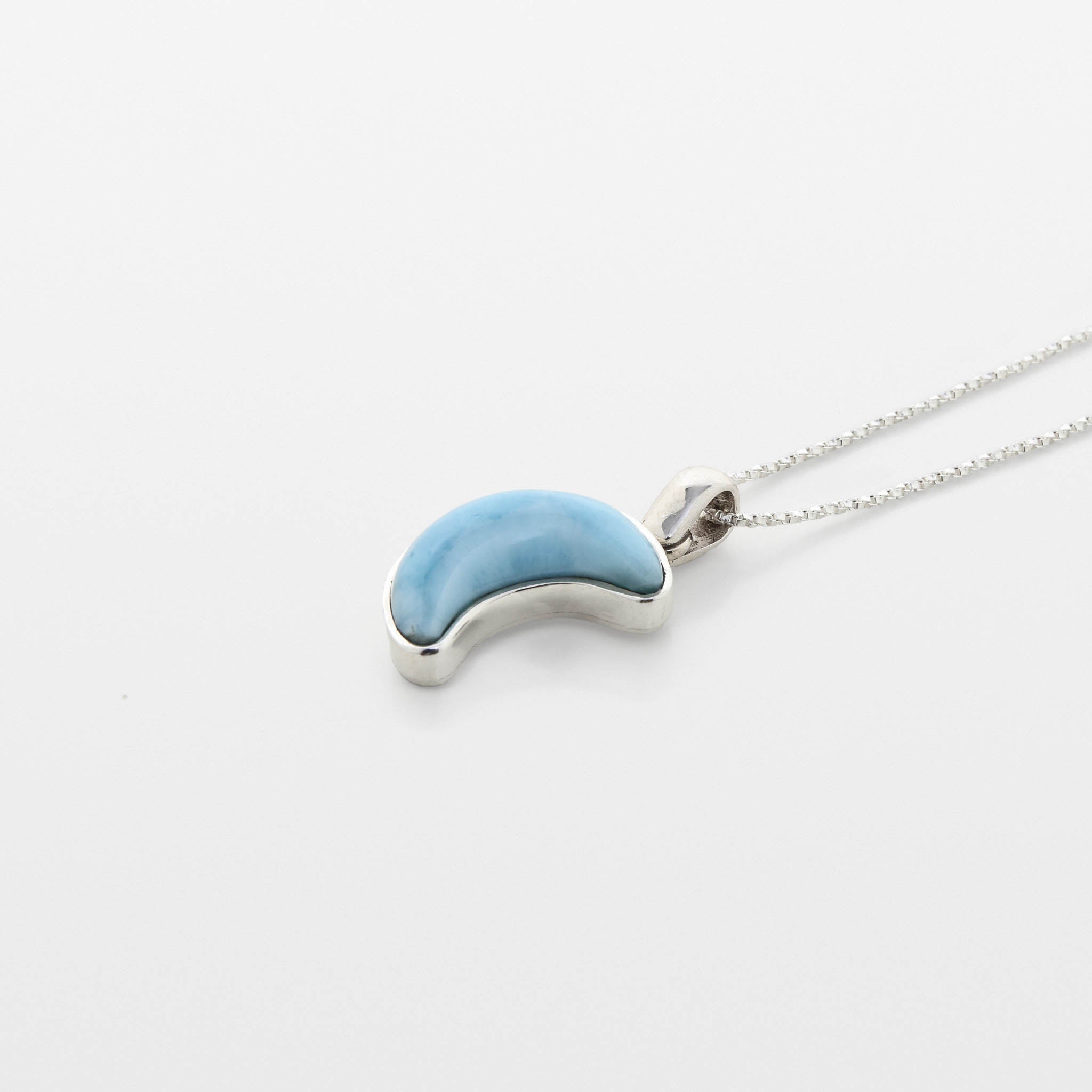 Blue Larimar crescent moon pendant on a silver chain against a white background