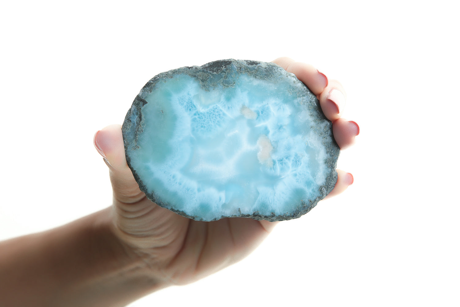 Hand holding a raw Larimar stone slab showing natural blue and white patterns, sourced from Barahona, Dominican Republic.