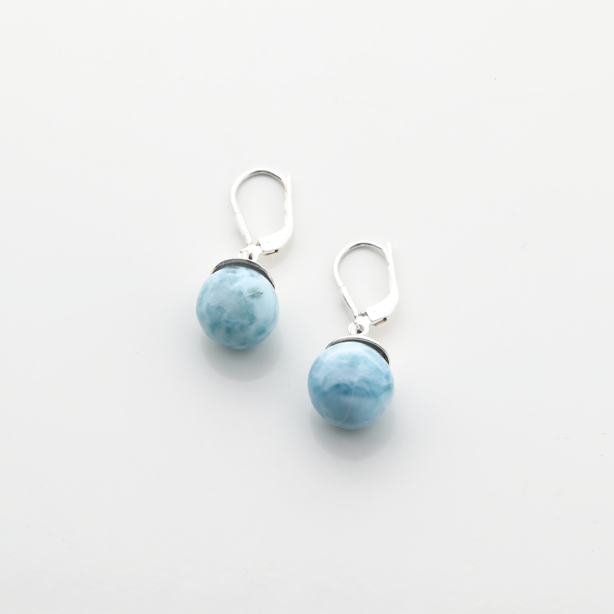 Stunning larimar round bead dangle earrings with silver hooks, perfect for any occasion. The light blue larimar stones are elegantly displayed, creating a unique and eye-catching accessory. Handcrafted with care, these earrings are a must-have addition to your jewelry collection.